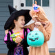 Two kids in Halloween costumes smiling while holding YumEarth candy and a teal pumpkin pail.
