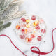 Colorful YumEarth lollipops on a white plate with holiday ribbon and pine branches.