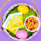 Easter basket with YumEarth jelly beans and colorful eggs on green grass and purple background.